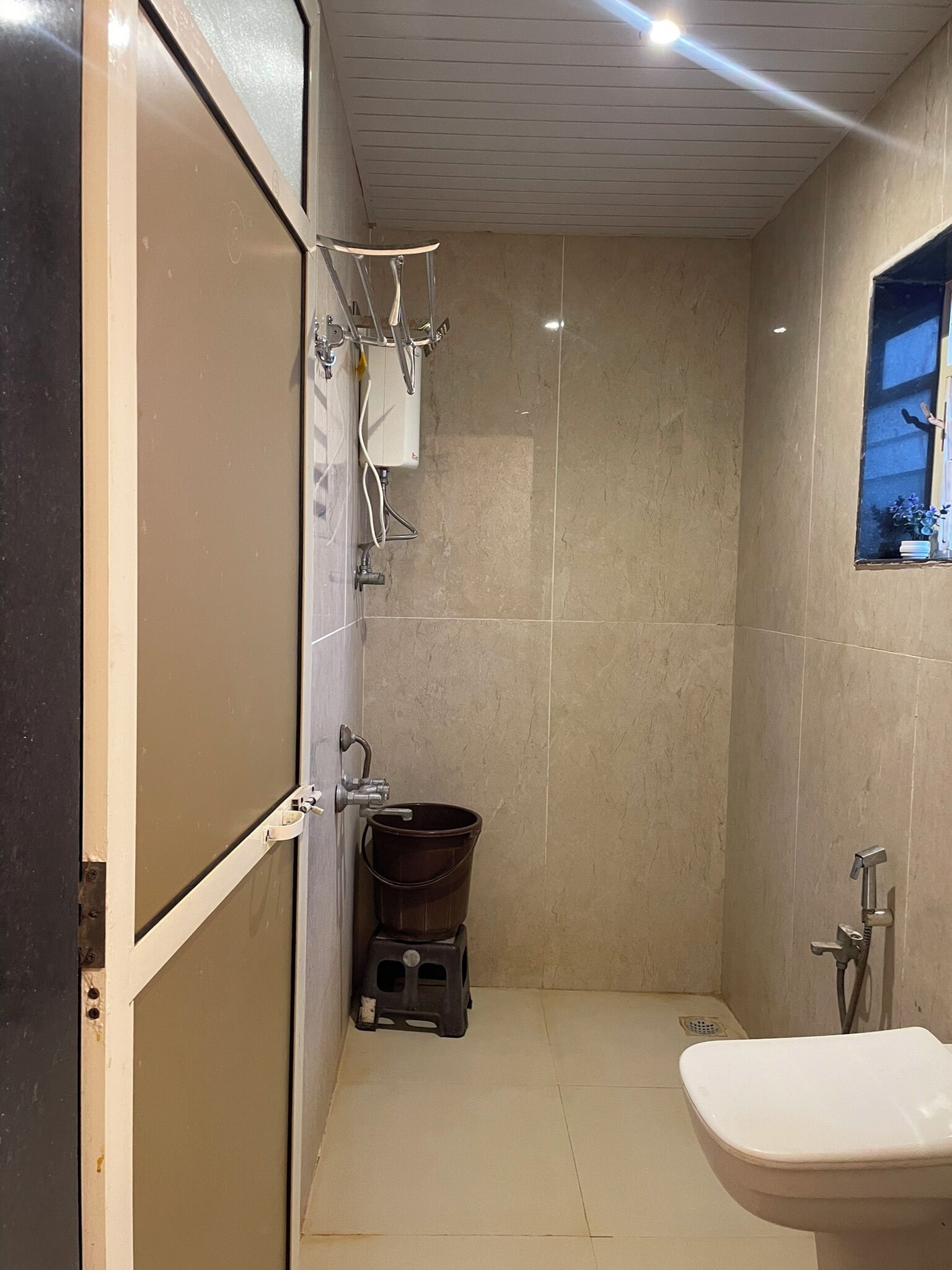 A small, tiled bathroom with a toilet, a shower area, and a window.