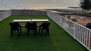 En træterrasse med et bord og stole med udsigt over stranden.