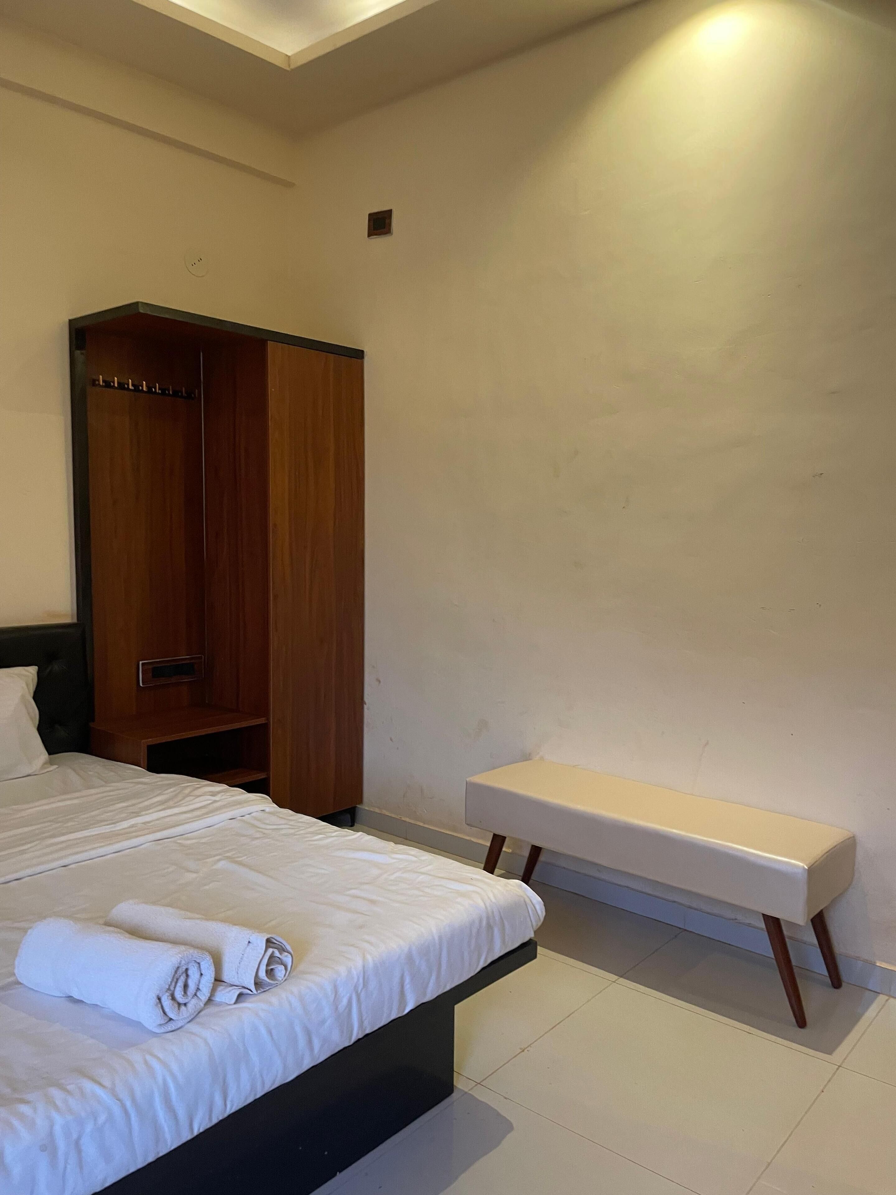 A bedroom with a bed, a wooden wardrobe, a bench, and a small table.