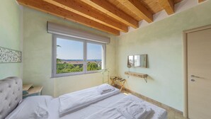 Une chambre à coucher avec un lit, une fenêtre donnant sur un beau paysage, un plafond en bois et une porte.
