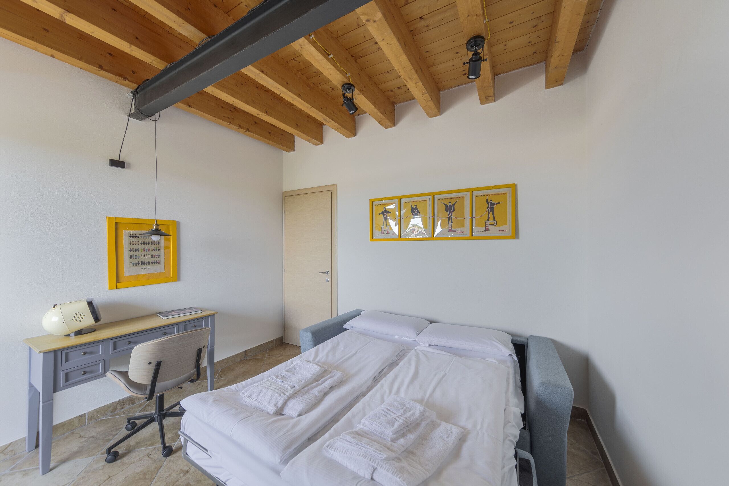 Une chambre avec un lit, un bureau et une chaise. Des tableaux encadrés ornent le mur.