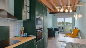 Une cuisine avec des meubles de couleur verte, un plafond en bois et un coin repas avec des chaises jaunes.