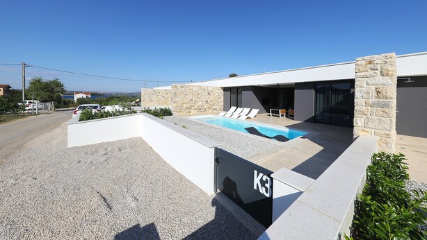 Ein modernes Haus mit Swimmingpool, Steinmauern und freiem Blick auf das Meer.