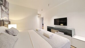 Ein modernes Hotelzimmer mit einem großen Bett, einem Flachbildfernseher, einem Nachttisch und einem an der Wand befestigten Fernseher.