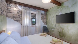 A bedroom with a stone wall, a bed with white bedding, a chair, and a flat-screen TV mounted on the wall. - Prisedi in Rakalj With 4 Bedrooms and 3 Bathrooms (Marcana)