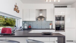 A modern kitchen with white cabinets, a black countertop, a built-in oven, and a window overlooking greenery. - Elsa in Krnica With 4 Bedrooms and 4 Bathrooms (Marcana)
