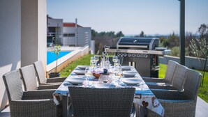 An outdoor dining area with wicker chairs and a table set for a meal, overlooking a swimming pool and a barbecue grill. - Elsa in Krnica With 4 Bedrooms and 4 Bathrooms (Marcana)