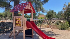 A wooden play structure with a red slide, surrounded by gravel and trees. - Sonia Hvar in Rudina Hvar (Stari Grad)