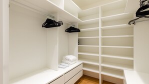 A walk-in closet with white shelving, a bench with folded towels, and hanging clothes.