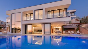 A modern two-story house with a swimming pool, large windows, and outdoor seating.