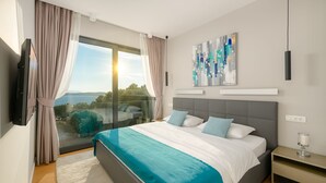 A modern bedroom with a large bed, a TV, a painting, and a view of the outdoors.