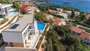 A modern house with a rooftop pool, surrounded by lush greenery and a coastal view.