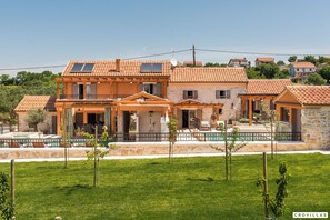 A two-story house with a tiled roof, a balcony, and a small garden area.