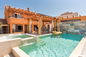 Ett poolområde med en pergola av trä, en bubbelpool och en mur av sten.