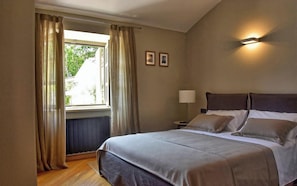Et hotelværelse med seng, natbord, lampe og et vindue med gardiner.