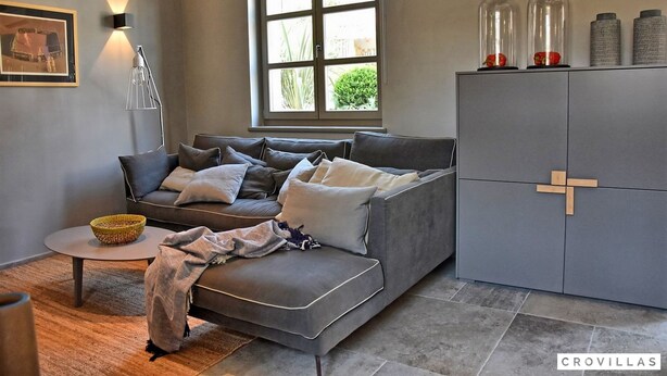 A modern living room with a grey sofa, a small round table, a lamp, and a window with a view of greenery. - Zita in Jakomi i With 5 Bedrooms and 5 Bathrooms (Pican)