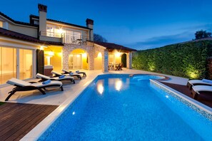 A swimming pool with lounge chairs, a stone building with a balcony, and a well-lit outdoor area.