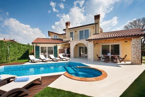 A two-story house with a swimming pool, outdoor seating, and a stone wall.