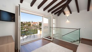 A modern room with a large sliding glass door leading to an outdoor patio, a flat-screen TV mounted on the wall, and a staircase with glass railings. - Santa Domenica in Labinci (Kastelir-Labinci)