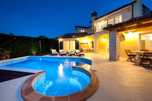A swimming pool with a hot tub, lounge chairs, and a dining area with outdoor seating.