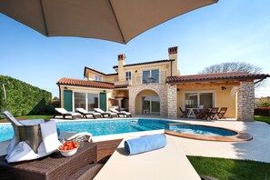 A poolside area with lounge chairs, a hot tub, and a stone building in the background.