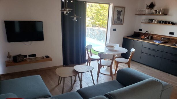 A modern living room with a sofa, a dining table with chairs, a kitchen area, and a TV mounted on the wall. - Lux V in Murter With 2 Bedrooms and 1 Bathrooms (Tisno)