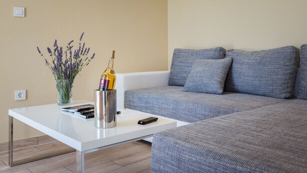 Un salón moderno con una mesita de centro blanca, un jarrón con lavanda, una botella de vino y un control remoto.