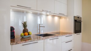 Una cocina moderna con gabinetes blancos, encimera de granito, pileta de acero inoxidable y horno empotrado.