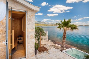 A stone building with a wooden sauna room, a hot tub, and a view of a lake. - Nick in Posedarje With 1 Bedrooms and 1 Bathrooms (Posedarje)