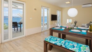 Un comedor con una mesa dispuesta para cuatro personas, un banco y vista al mar a través de puertas de cristal.