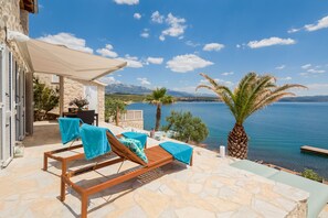 A stone patio with lounge chairs and a table, overlooking a body of water and mountains. - Nick in Posedarje With 1 Bedrooms and 1 Bathrooms (Posedarje)
