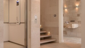 Un ascensor moderno con pantalla digital, una escalera de mármol y una pared de piedra con un lavabo.