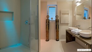 Un baño moderno con cabina de ducha de vidrio, dos lavamanos y esculturas de madera decorativas.
