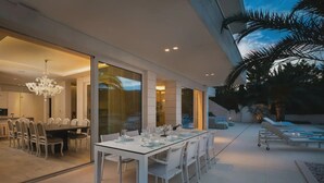 Un comedor moderno con una gran mesa y sillas, una lámpara de araña y vistas al patio exterior.
