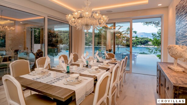 Un comedor con una araña, sillas blancas y una mesa dispuesta para una comida.