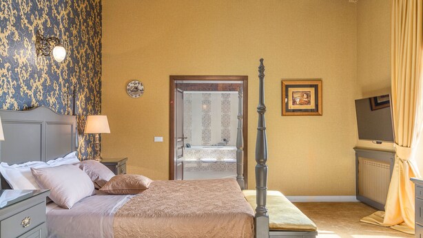 A bedroom with a four-poster bed, a nightstand with a lamp, a dresser, a television, and a bathroom visible through an open door. - Carolus in Barat With 5 Bedrooms and 5 Bathrooms (Visnjan)