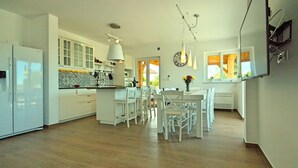Una cocina moderna con armarios blancos, un comedor con sillas blancas y un amplio ventanal que proporciona luz natural.
