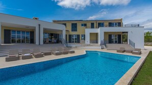 A modern two-story house with a swimming pool, outdoor seating, and a clear blue sky. - Arkaim in Filipana With 5 Bedrooms and 5 Bathrooms (Marcana)