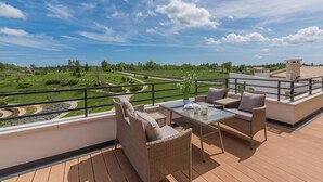 A balcony with wicker furniture, a glass table, and a view of a green landscape. - Arkaim in Filipana With 5 Bedrooms and 5 Bathrooms (Marcana)