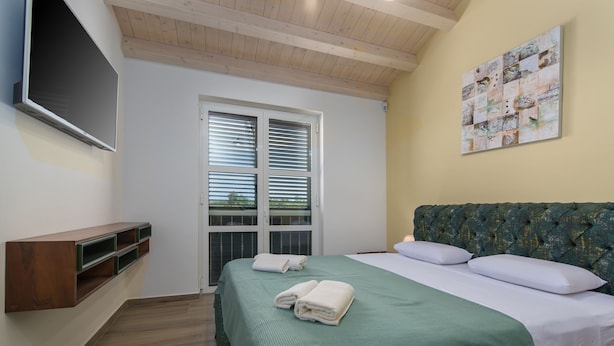 A bedroom with a bed, a TV mounted on the wall, a window with blinds, and a painting on the wall. - Arkaim in Filipana With 5 Bedrooms and 5 Bathrooms (Marcana)