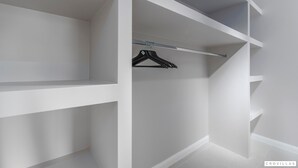 Un placard blanc avec plusieurs étagères et une seule tringle pour suspendre les vêtements.