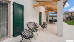 Une terrasse extérieure avec des poutres en bois, un espace salon couvert et une vue sur un bâtiment en pierre en arrière-plan.