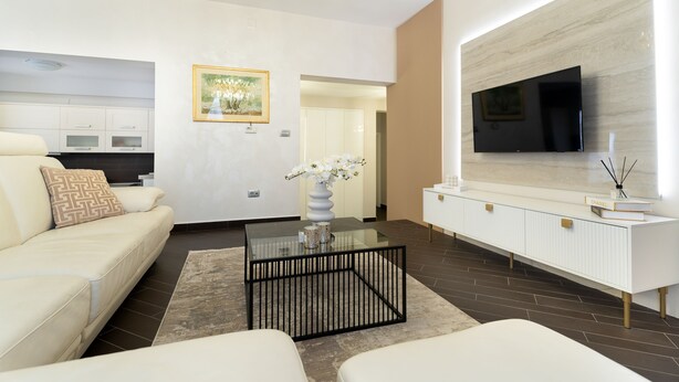 Un salon moderne avec une table basse en verre, des canapés blancs, un téléviseur à écran plat et un design minimaliste.