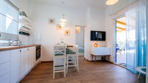 A modern kitchen with white cabinets, a wooden countertop, and a dining area with white chairs. - Muntan in Kraj With 2 Bedrooms and 2 Bathrooms (Pasman)