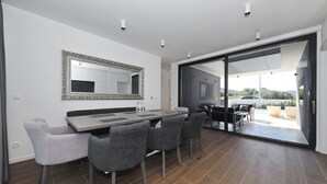 A modern dining area with a large table and chairs, a decorative mirror, and a sliding glass door leading to an outdoor seating area. - K1 in Kraj With 3 Bedrooms and 1 Bathrooms (Pasman)