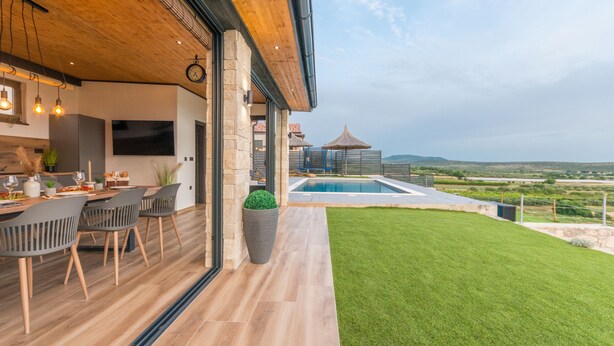 A modern kitchen with a dining area, a large potted plant, and a view of a swimming pool and landscape. - La Vrana in Vrana With 3 Bedrooms and 2 Bathrooms (Pakostane)