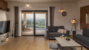 A modern living room with a large TV, two sofas, a coffee table, and a view through a glass door to a balcony. - La Vrana in Vrana With 3 Bedrooms and 2 Bathrooms (Pakostane)