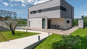 A modern two-story building with a stone facade, a small patio with outdoor seating, and a clear sky. - Callista in Ru i i (Sveta Nedelja)