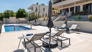 A rooftop pool area with lounge chairs and umbrellas, a swimming pool, and a modern building with balconies. - Callista in Ru i i (Sveta Nedelja)