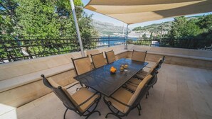 An outdoor patio with a table and chairs, a canopy, and a view of a bridge and hills. - Franica in Dubrovnik (Dubrovnik)